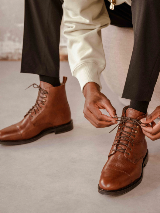 A man ties the laces on his brown formal shoes.