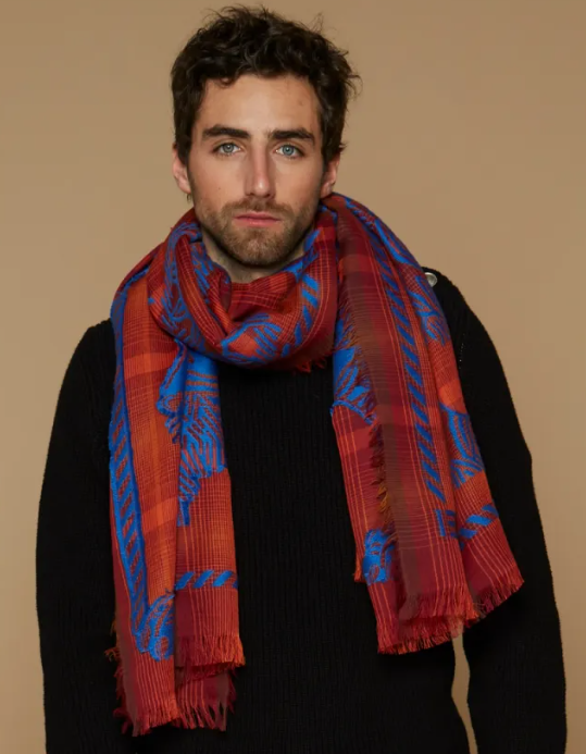 A dark-haired man looks ahead wearing a red and blue colored scarf.