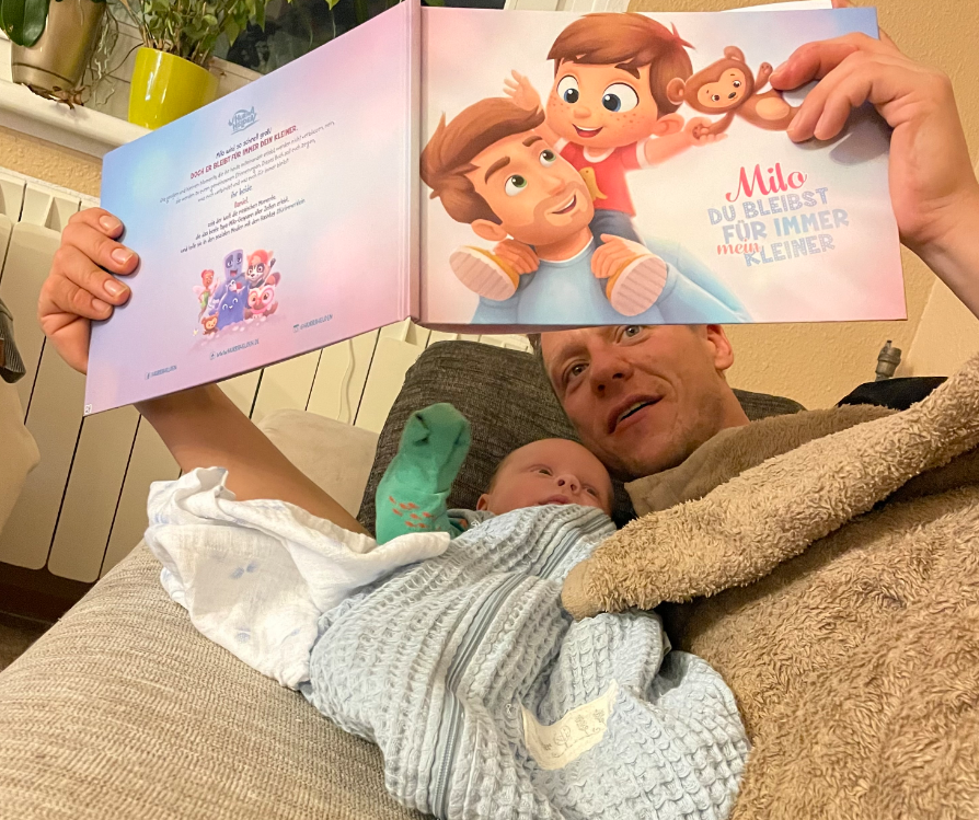 A dad expectig his baby to say 'Dad' very soon, while reading a personalized book.