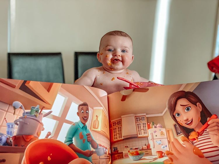 A baby covered in food sitting behind his own custom book for new parents.